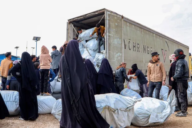عائلات في مخيم «الهول» شمال شرقي سوريا أمام شاحنة حاويات تحمل أمتعتهم استعداداً للمغادرة إلى العراق (أرشيفية - أ.ف.ب)