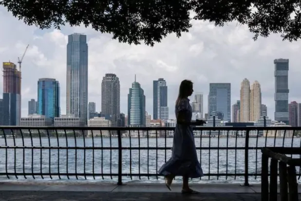امرأة تمشي على طول نهر هدسون مع أفق جيرسي سيتي في الخلفية بمدينة نيويورك (رويترز)