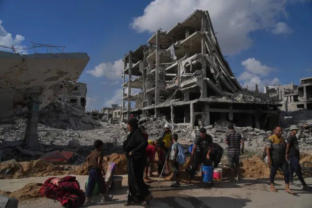 فلسطينيون يجمعون المياه من أنبوب مكسور يحيط بالمباني المدمَّرة في مدينة غزة أمس (أ.ب)