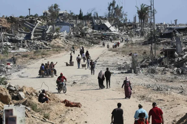 فلسطينيون نازحون يسيرون أمام المباني المدمرة في أثناء عودتهم إلى منازلهم شمال مخيم النصيرات للاجئين في وسط قطاع غزة (أ.ف.ب)