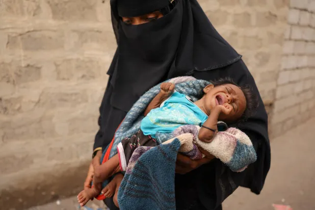 يمنية تحمل طفلها الذي يعاني من سوء التغذية في الخوخة جنوبي الحديدة (رويترز)