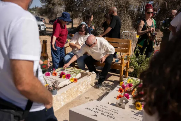 İsrail'in güneyindeki Gazze sınırına yakın Kfar Aza yerleşiminde yakınlarının mezarlarının yanında duran aileler (AFP)