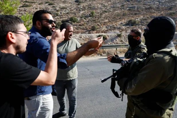 فلسطينيون يحتجون أمام جنود إسرائيليين على عملية توسيع الطريق لربط المستوطنات الإسرائيلية بالضفة الغربية (رويترز)