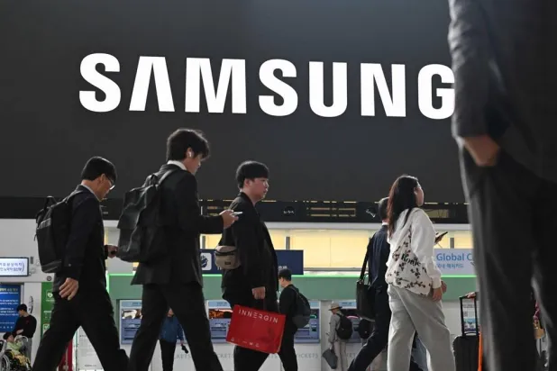 People walk past a large electronic screen showing the Samsung logo at Seoul train station in Seoul on October 14, 2025. (AFP)