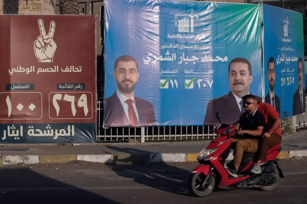 شخصان يقودان دراجتهما البخارية أمام لوحات إعلانية انتخابية في أحد شوارع بغداد (أ.ف.ب)