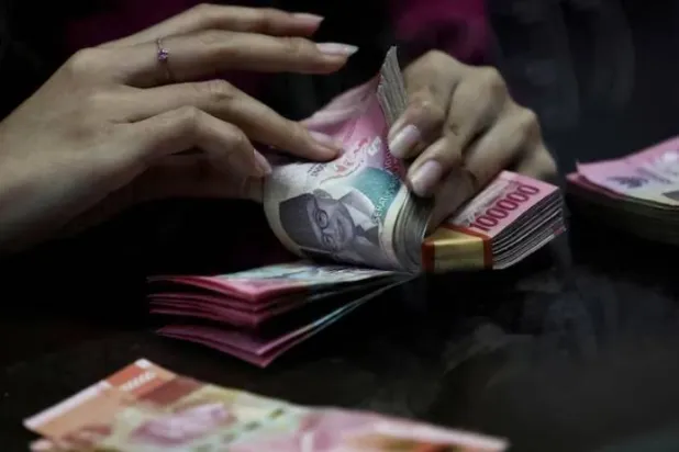 أحد الصرافين يعد أوراق نقدية بالروبية في محل صرافة في جاكرتا (رويترز)