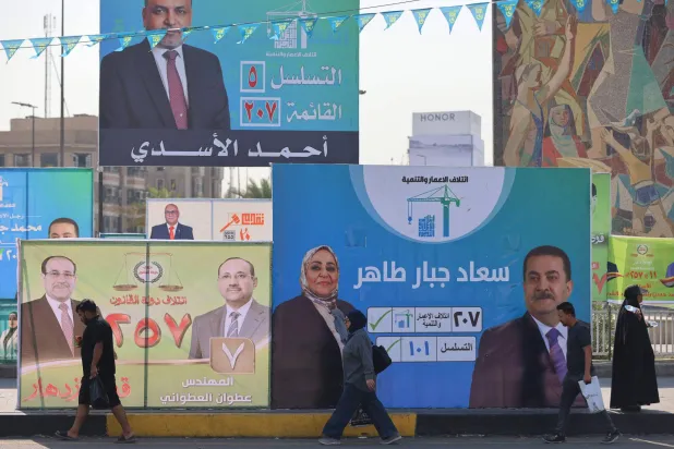 مارة يعبرون أمام لوحات انتخابية في وسط بغداد (أ.ف.ب)