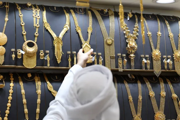 عارِض يعرض قطعة من الذهب على أحد الزبائن بمتجر مجوهرات داخل سوق الذهب في دبي (إ.ب.أ)