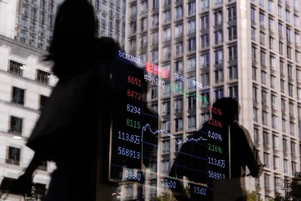 مارة يسيرون أمام مركز للتداول في الضاحية المالية بالعاصمة الصينية بكين. بينما يبدو على الزجاج انعكاس شاشة إلكترونية تعرض حركة الأسهم (رويترز)