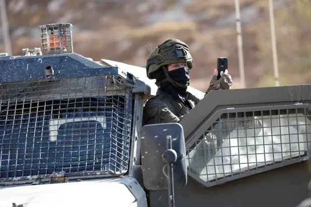 A member of the Israeli force uses a mobile phone as Israeli forces block the access of Palestinians and foreign activists to olive trees during the olive harvest, near Hebron, in the Israeli-occupied West Bank, October 23, 2025. REUTERS/Mussa Qawasma