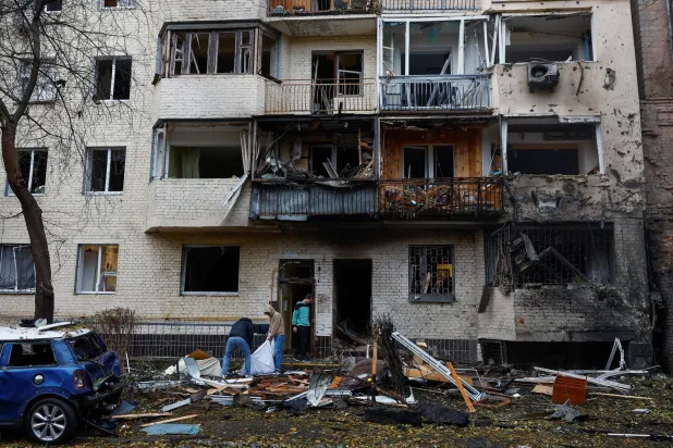 سكان يُخرجون الحطام من شقتهم التي تضررت خلال غارة جوية روسية على كييف (رويترز)