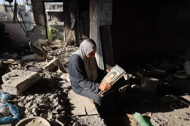 فلسطينية تمعن النظر في صورة والدها وسط ركام بيتها الذي عادت إليه في مخيم البريج بوسط قطاع غزة يوم الخميس (أ.ف.ب) 