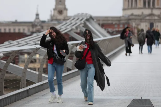 People laugh as they cross Millennium Bridge during high winds brought by Storm Benjamin, in London, Britain, October 23, 2025. REUTERS/Corey Rudy