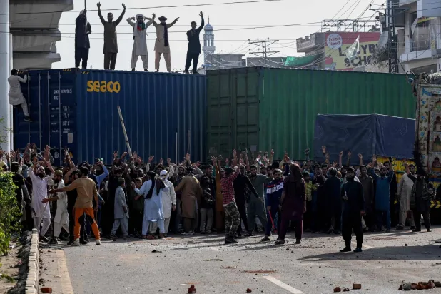 نشطاء من حزب حركة «لبيك باكستان» يهتفون بشعارات قرب مقرهم بينما أغلقت السلطات الطريق بحاويات شحن في لاهور في 9 أكتوبر 2025 قبل انطلاق مسيرتهم المؤيدة للفلسطينيين باتجاه إسلام آباد (أ.ف.ب)