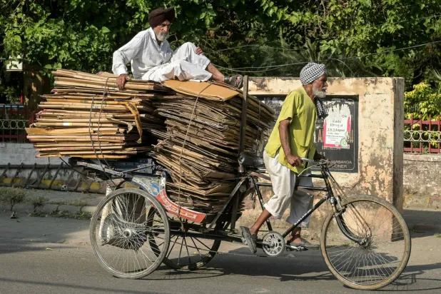 رجل على دراجة حاملاً حزمة من الورق المقوى يمر في أحد شوارع ولاية أمريستار الهندية (أ.ف.ب)
