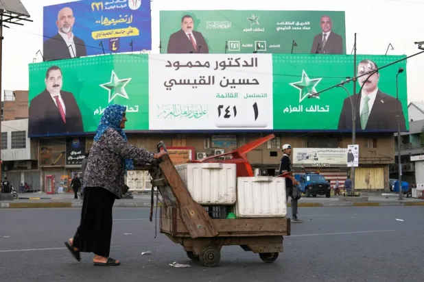 A woman pushes a cart past a banner for Iraq’s parliamentary elections in Baghdad (AP)
