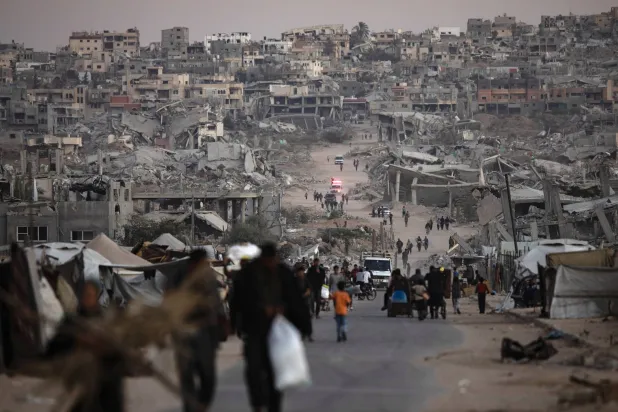 فلسطينيون يسيرون بين أنقاض منازلهم المدمَّرة في خان يونس بجنوب قطاع غزة (إ.ب.أ)