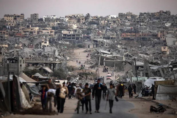 فلسطينيون يسيرون وسط المباني المدمرة في خان يونس بجنوب قطاع غزة (إ.ب.أ)