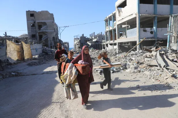 امرأة فلسطينية نازحة وعائلتها يسيرون بين أنقاض منزلهم المدمر في مخيم الشاطئ للاجئين بمدينة غزة (رويترز)