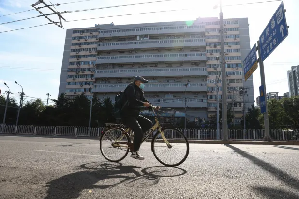 رجل مُسن يركب دراجة أمام مبنى سكني في بكين (إ.ب.أ)
