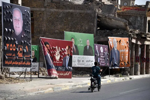 رجل يقود دراجته الهوائية أمام ملصقات تُظهر مرشحين للانتخابات العراقية بمدينة الموصل القديمة (أ.ف.ب)