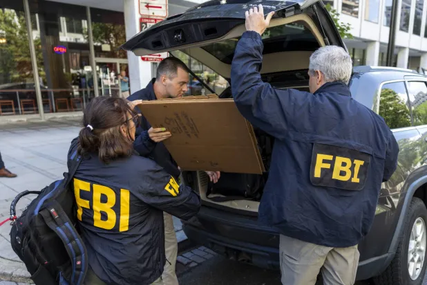 عملاء مكتب التحقيقات الفيدرالي يغادرون مكتب جون بولتون مستشار الأمن القومي السابق للرئيس الأميركي دونالد ترمب في واشنطن (إ.ب.أ)