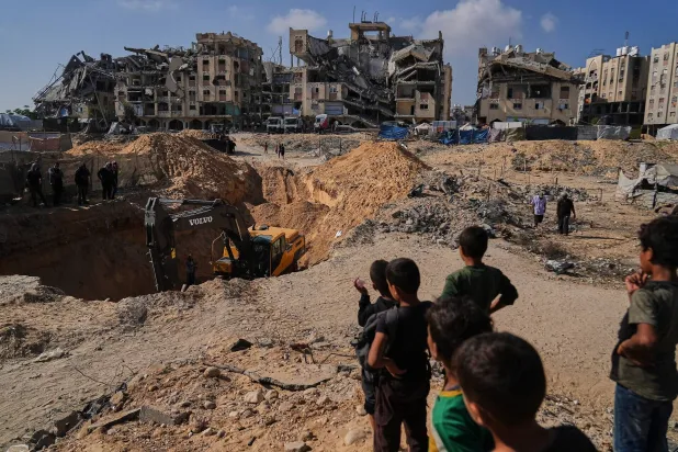 فلسطينيون يراقبون آلات وعمالاً مصريين خلال بحثهم عن جثث رهائن في مدينة حمد بخان يونس جنوب قطاع غزة 28 أكتوبر 2025 (أ.ب)