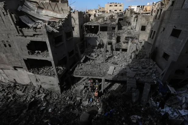 فلسطينيون يفحصون الدمار بين أنقاض المنازل المدمرة إثر غارة جوية إسرائيلية استهدفت مبنى سكني في مخيم الشاطئ للاجئين بمدينة غزة (إ.ب.أ)