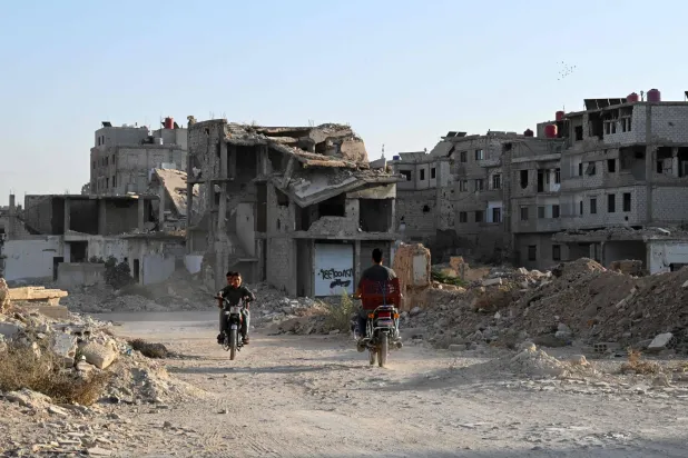 أشخاص يركبون دراجاتهم النارية أمام مبان مدمرة في داريا على مشارف دمشق في 28 أكتوبر 2025 (أ.ف.ب)
