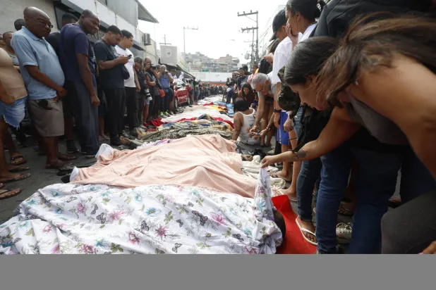 مواطنون برازيليون ينظرون إلى جثثٍ جُمعت في أحد شوارع ريو دي جانيرو الأربعاء (إ.ب.أ)