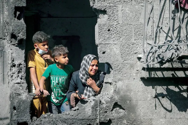  طفلان فلسطينيان وأمهما يطلون من منزلهم المدمر إثر غارة جوية إسرائيلية استهدفت مخيم الشاطئ للاجئين بمدينة غزة (إ.ب.أ)