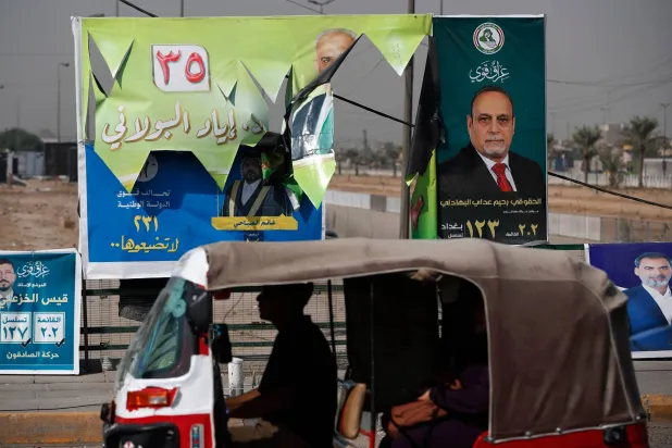 سيارة تمر أمام ملصقات انتخابية في مدينة الصدر شرق بغداد استعداداً للانتخابات البرلمانية (أ.ف.ب)