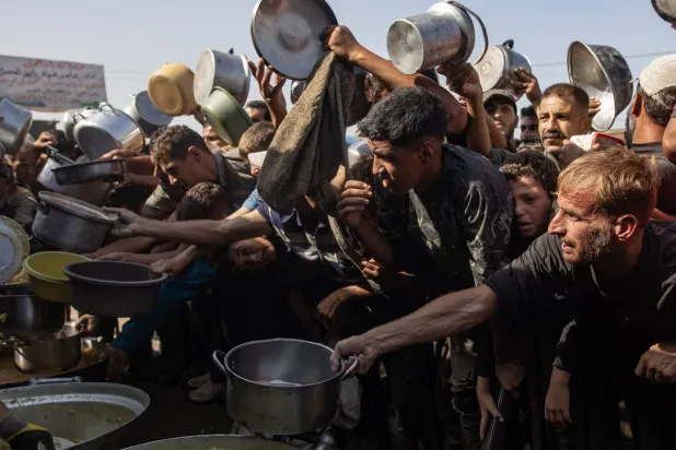 نازحون فلسطينيون يحاولون الحصول على وجبة طعام في مطبخ خيري بخان يونس جنوب قطاع غزة الجمعة (إ.ب.أ)