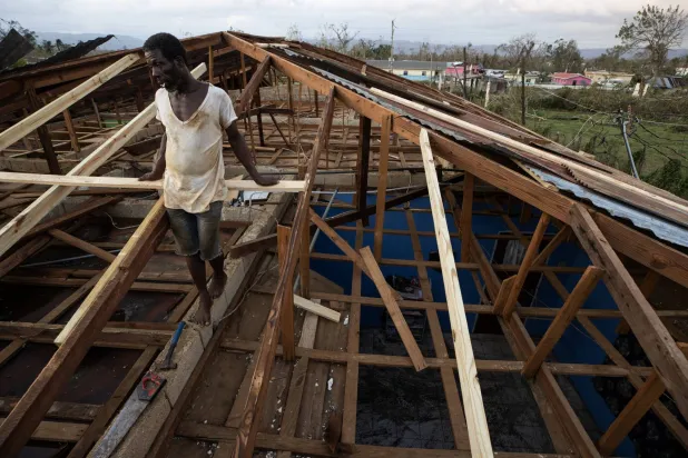 رجل يعمل على إصلاح سطح منزل في سانتا كروز بجامايكا (إ.ب.أ)