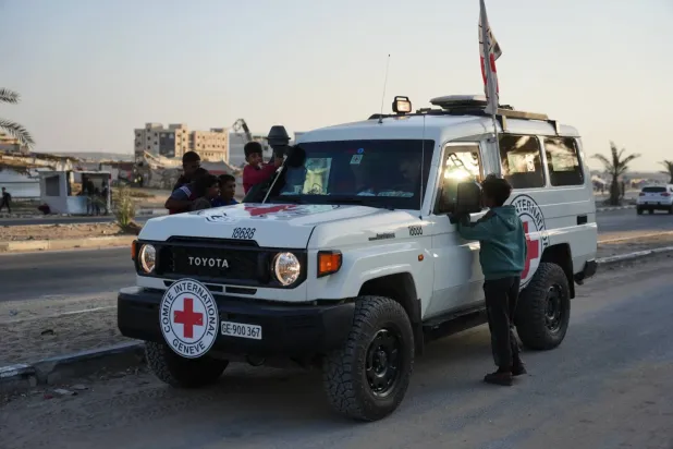 Filistinli çocuklar, perşembe günü Gazze Şeridi'nin merkezindeki Deyr el-Belah'ta İsrail makamlarına teslim edilmek üzere, Hamas tarafından rehin alınan ve öldüğü düşünülen iki kişinin cesetlerini taşıyan Kızılhaç araçlarını inceliyorlar (AP)