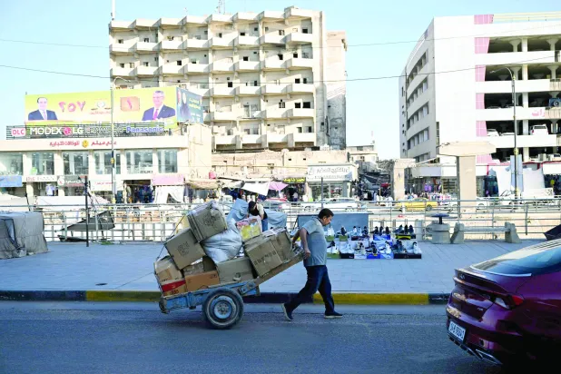 مردی در حال کشیدن چرخ‌دستی در برابر پوسترهای تبلیغات انتخاباتی پیش از برگزاری انتخابات پارلمانی در بصره، جنوب عراق (فرانس‌پرس)