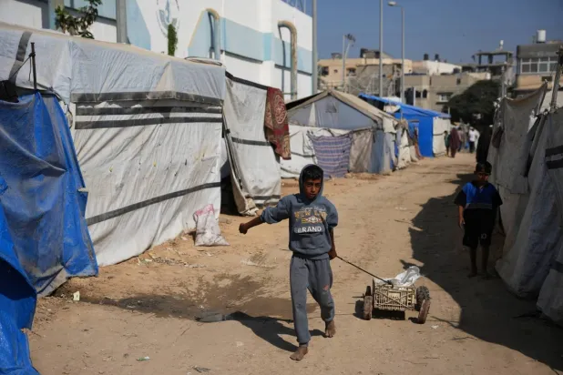 A Palestinian boy pushes a cart loaded with water containers in a displacement camp in Deir al-Balah, central Gaza, on Saturday (AP Photo)
