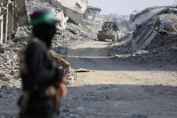 عنصر من «حماس» يقف بمدينة غزة قرب «الخط الأصفر» بينما تعمل آلية على البحث عن جثامين رهائن إسرائيليين يوم الأحد (رويترز)
