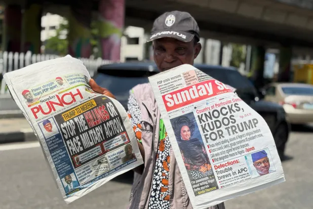 بائع يحمل صحفاً تستعرض تهديد ترمب بتدخل عسكري لحماية مسيحيي نيجيريا في لاغوس يوم 2 نوفمبر (أ.ب)