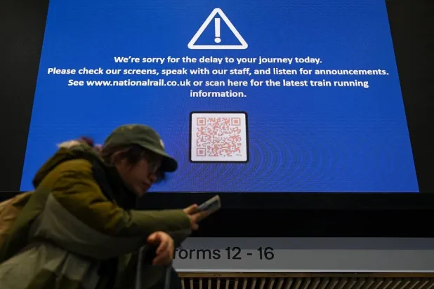 A person looks at a phone next to a screen showing information on a rail service delay following a train derailment near Shap in Cumbria, at Euston Station in London, Britain, November 3, 2025. (Reuters)
