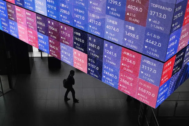 رجل يمشي بجانب لوحة عرض إلكترونية لأسعار مؤشر «نيكي 225» في بورصة طوكيو (أ.ف.ب)