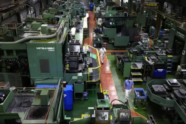 عمال يسيرون بين آلات دقيقة لتصنيع قطع غيار السيارات داخل مصنع شركة «كيوا» الصناعية في تاكاساكي (رويترز)