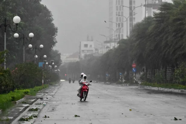 سائقون يركبون دراجة في ظل رياح قوية قبل وصول الإعصار «كالمايغي» على طريق بالقرب من شاطئ كوي نون وسط فيتنام (أ.ف.ب)