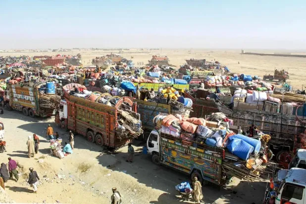 Afgan mülteciler, Pakistan sınırına yakın Chaman'da Afganistan'a sınır dışı edilmek üzere eşyalarını taşıyan kamyonların önünde bekliyorlar (AFP)