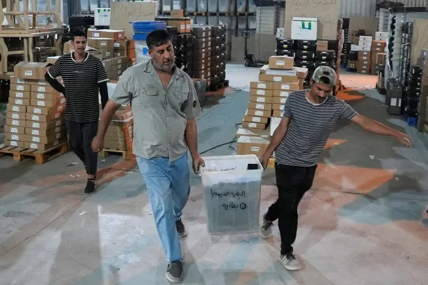 موظفون من مفوضية الانتخابات العراقية ينقلون صندوق اقتراع داخل مستودع في البصرة (رويترز)