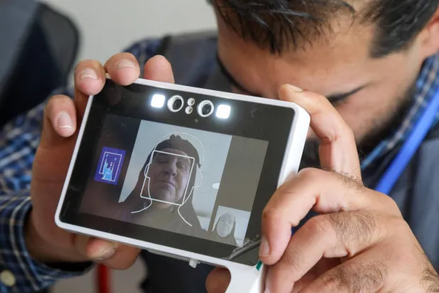 موظف انتخابي يلتقط صورة بطاقة هوية لامرأة عراقية نازحة لدى وصولها للتصويت في مخيم ديبكة شمالي العراق (أ.ف.ب)