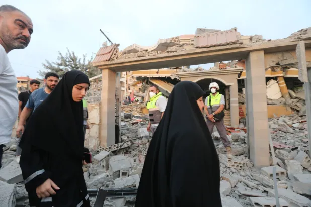 لبنانيون يسيرون قرب مبنى دمرته غارة إسرائيلية الخميس في بلدة طيردبا بجنوب لبنان (إ.ب.أ)