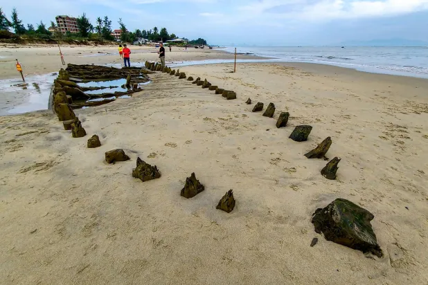 People stand next to a centuries-old shipwreck uncovered in the aftermath of Typhoon Kalmaegi on a beach off the Hoi An coast in central Vietnam, on November 10, 2025. (Photo by Tam Xuan / AFP)