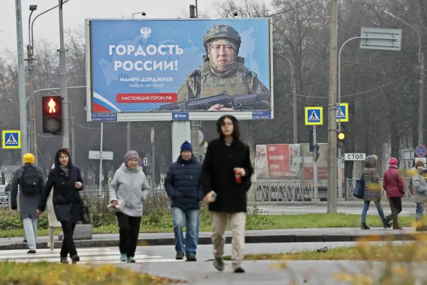 مواطنون روس يسيرون في أحد شوارع سان بطرسبورغ وخلفهم ملصق ضخم يصور جندياً مع كلام يقول: «فخر روسيا» (إ.ب.أ)