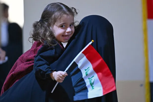 ناخبة عراقية تحمل طفلها حاملاً علم البلاد في مركز اقتراع بمدينة البصرة الجنوبية (أ.ف.ب)
